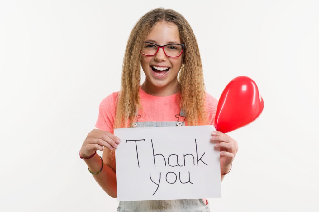 A teenage girl holding a paper with a thank you text, and a heart balloon